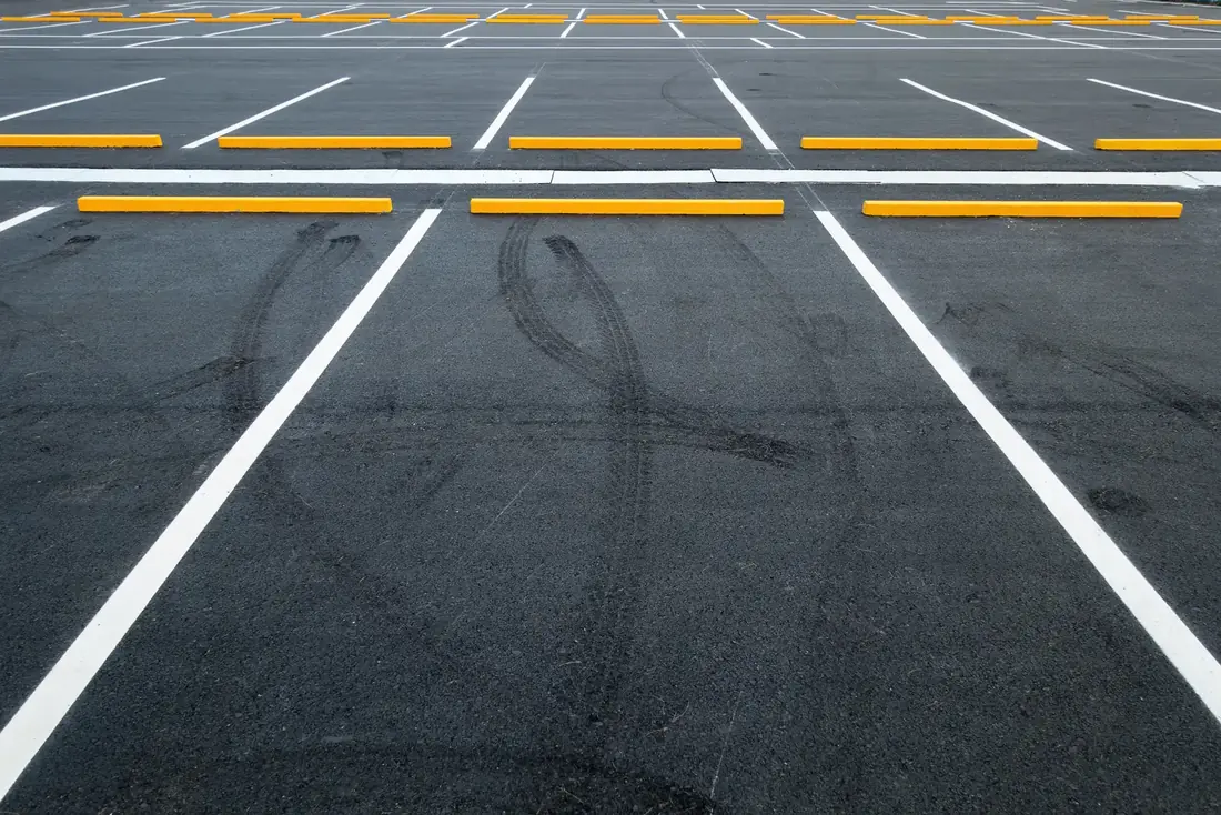 Freshly painted white parking stall lines and yellow wheel stops on dark asphalt in a commercial parking lot
