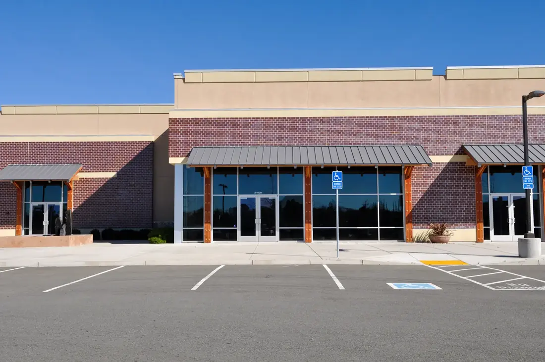 Commercial storefront parking lot with striped stalls, a blue accessible parking symbol, a hatched access aisle and an accessible parking sign